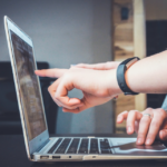 Two people pointing at a laptop screen discussing the benefits of implementing proposal automation solutions.