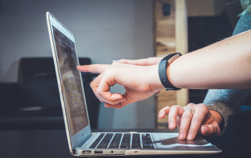 Two people pointing at a laptop screen discussing the benefits of implementing proposal automation solutions.